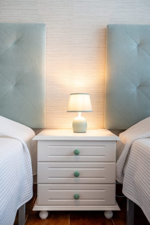 Luminária de cabeceira em criado-mudo branco entre duas camas com cabeceiras acolchoadas no apartamento Pêra Breeze
