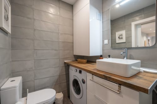 Banheiro moderno do apartamento Pêra Breeze no Happy Nest AL com cuba branca, azulejos cinza, máquina de lavar e espelho