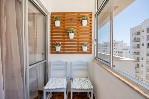 Varanda do apartamento Happy Nest AL em Armação de Pêra com duas cadeiras azuis, parede verde com plantas e vista para a cidade do Algarve