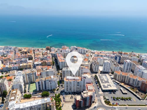 Vista aérea da vila costeira de Armação de Pêra com águas turquesas e edifícios brancos