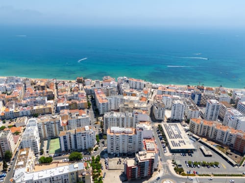 Vista aérea da vila costeira de Armação de Pêra com praia turquesa e edifícios brancos
