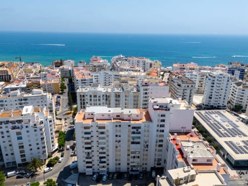 Vista aérea da localidade costeira de Armação de Pêra com edifícios brancos e mar turquesa