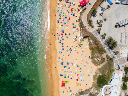 Vista aérea da praia de Armação de Pêra com guarda-sóis coloridos e banhistas na areia
