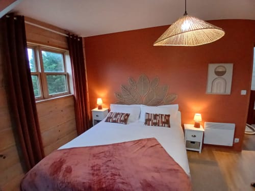 Chambre douillette à Ma Cabane du Canada à Combray avec murs orange, lit blanc, parquet et luminaires suspendus modernes