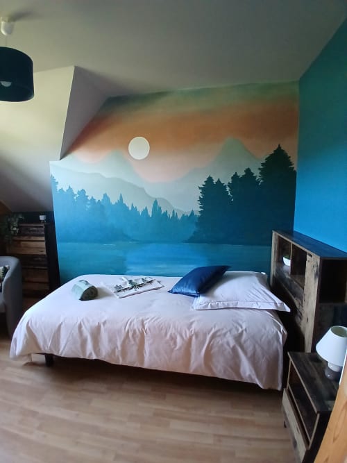 Chambre avec lit blanc et oreiller bleu face à une fresque murale de lac de montagne avec silhouettes de forêt à Ma Cabane du Canada, Vancouver