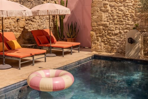 Le Prieuré Notre-Dame courtyard pool with pink inflatable, loungers under umbrellas, stone walls in Montfrin