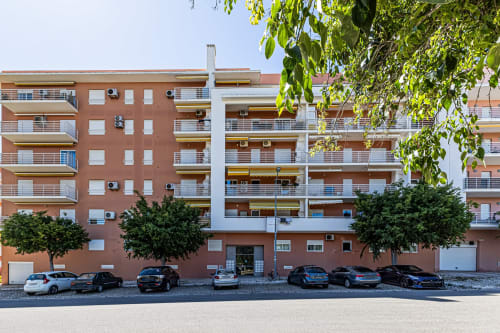 Fachada de edifício moderno em Armação de Pêra com carros estacionados e paisagismo verde