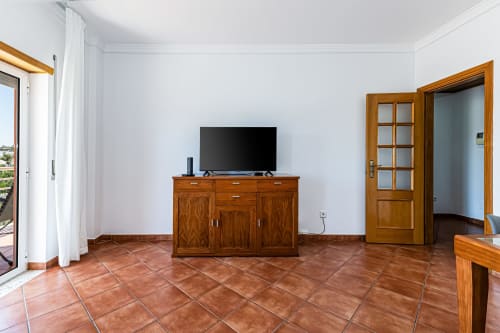 Sala de estar do apartamento Mar Azul com móvel de TV em madeira, piso em cerâmica terracota e acesso à varanda em Happy Nest AL, Armação