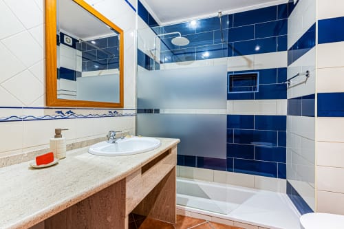 Banheiro moderno do apartamento Mar Azul da Happy Nest AL com chuveiro em azulejo azul e branco, lavatório em madeira e espelho em Armação