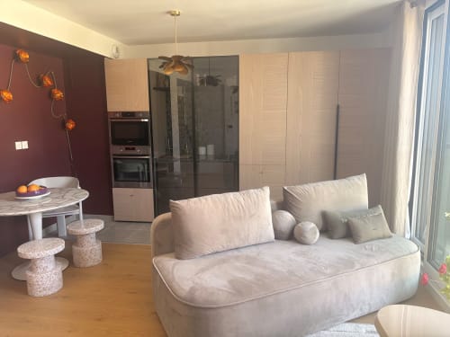Modern apartment living area at Maisons Valmer Le Havre with cream sofa, kitchen, burgundy accent wall, and sea view window