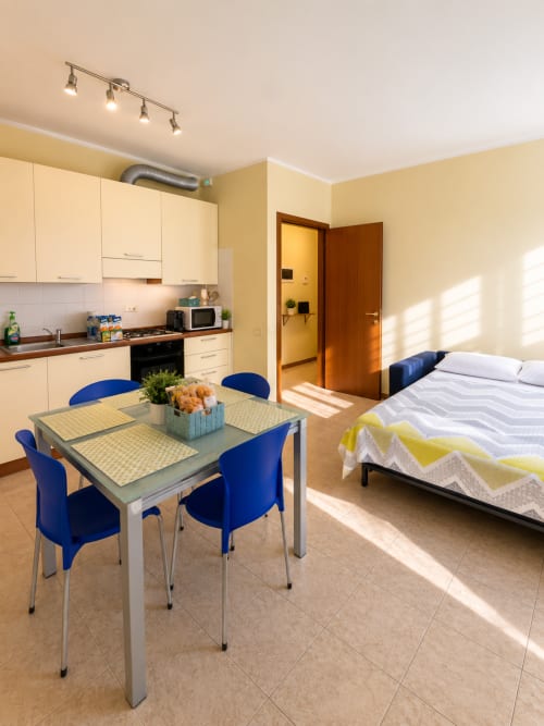 Monolocale a Bicocca, Milano con cucina, tavolo da pranzo, sedie blu e letto con luce naturale