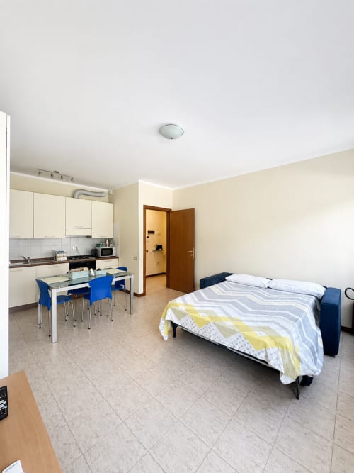 Monolocale a Bicocca Flat Milano con letto, angolo cottura, tavolo da pranzo e sedie blu su pavimento in ceramica