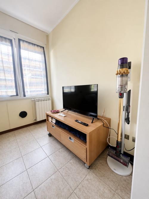 Soggiorno moderno dell'appartamento Bicocca Flat Milano con TV a schermo piatto, consolle in legno e aspirapolvere cordless