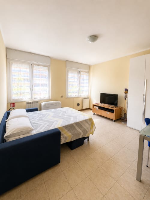 Spaziosa camera da letto dell'appartamento Bicocca Flat Milano con letto matrimoniale, TV, finestre e arredi moderni