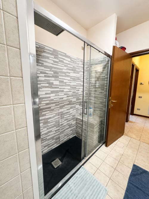 Moderno box doccia in vetro con piastrelle a righe grigie nel bagno dell'appartamento Bicocca Flat Milano