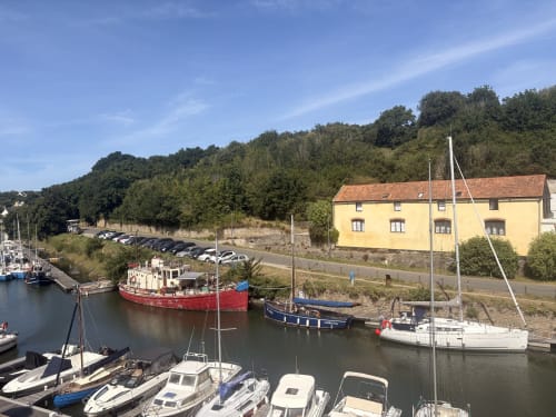 Sailboats moored at Le Havre marina with yellow building and wooded hills, Maisons Valmer view