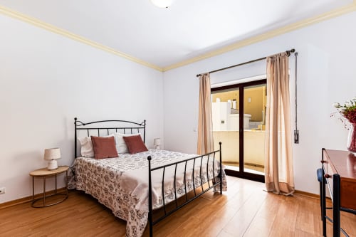 Quarto moderno no Happy Nest AL em Portimão com cama de estrutura metálica, piso de madeira e acesso a varanda com vista para a cidade