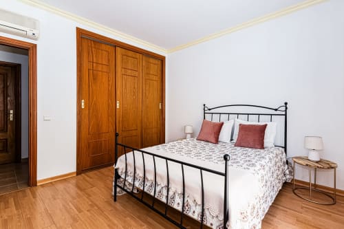 Quarto do Happy Nest AL em Portimão com cama de ferro preto, guarda-roupa de madeira e vista para a cidade