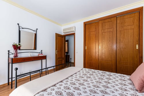 Quarto espaçoso da Happy Nest AL com guarda-roupa em madeira, penteadeira e cama estampada em Portimão