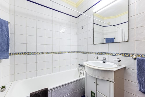 Banheiro moderno no Happy Nest AL em Portimão com azulejos brancos, pia oval, banheira, espelho e acentos em toalhas azuis