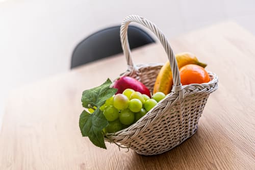 Cesto de vime com uvas frescas, maçã e frutas cítricas sobre mesa de madeira no apartamento Happy Nest AL em Portimão
