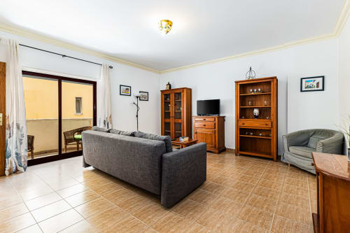 Sala de estar espaçosa no apartamento Happy Nest AL em Portimão com sofá cinzento, móveis em madeira, TV de ecrã plano e varanda