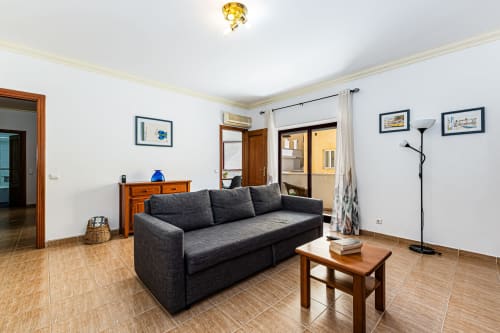 Sofá escuro em sala luminosa do Happy Nest AL Portimão com móveis de madeira e vista da cidade