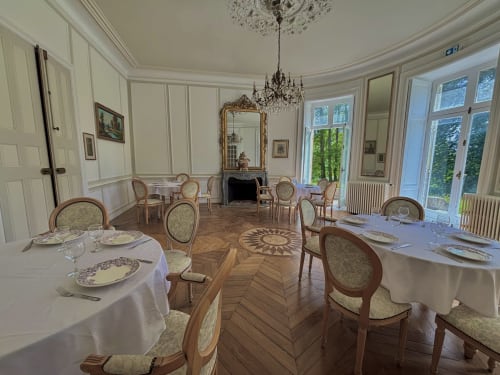 Salle à manger élégante au Château De Saint Thomas avec tables rondes, chaises ornées, lustre en cristal et cheminée