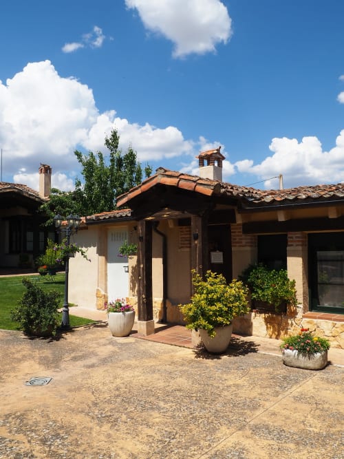 Rural Senda del Duratón Apartments courtyard in Sebúlcor with terracotta-roofed buildings, potted plants, and clear blue sky