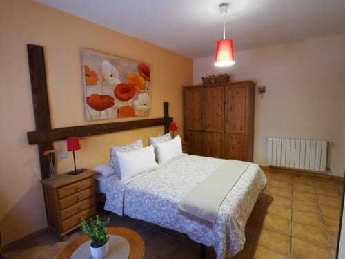 Dormitorio rústico en Apartamentos Senda del Duratón con cama de madera, ropa de cama azul, muebles de madera, lámpara colgante roja y