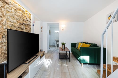Sala de estar moderna da pousada Happy Nest AL em Pêra com sofá verde, TV e parede de pedra com vista para o mar