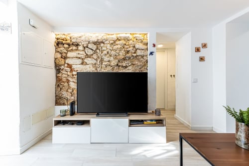 Sala de estar moderna da casa de hóspedes Happy Nest AL em Pêra, com TV de tela plana, móvel branco para mídia e parede de pedra aparente