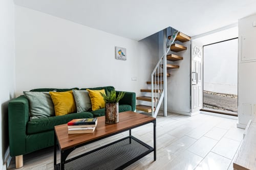 Sala de estar moderna com sofá verde, mesa de madeira e escada caracol na Casa Passarinho, Pêra