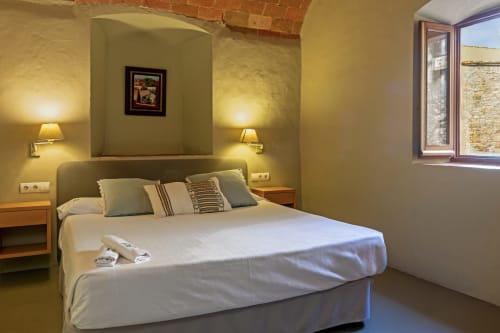 Dormitorio luminoso con cama blanca, paredes color oliva y vistas al jardín en Apartmentos Rectoria de Regencós, España