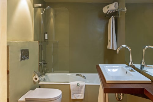 Baño moderno con doble lavabo, bañera con mampara de vidrio y paredes verde oliva en Apartmentos Rectoria de