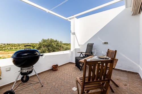 Terraço na cobertura da Casa Passarinho em Pêra com churrasqueira, mesa de refeições e vista para o campo