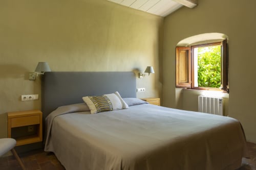 Chambre lumineuse avec tête de lit bleue, tables de nuit en bois et vue sur le jardin aux Apartmentos Rectoria de Regencós