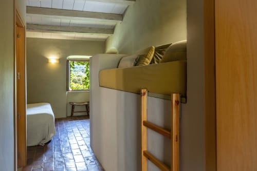 Chambre douillette avec lit mezzanine et échelle en bois aux Apartmentos Rectoria de Regencós, vue sur le jardin et poutres rustiques.