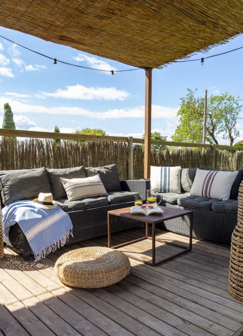Terrasse ombragée avec mobilier en rotin et coussins donnant sur le jardin de la maison Costa Brava