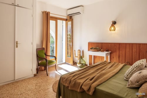 Chambre spacieuse à la Villa ANNONCIADE à Centuri avec tête de lit en bois, portes avec vue mer, fauteuil vert et climatisation