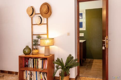 Entrée avec étagères en bois, chapeaux de paille, lampadaire et plantes en pot à la villa La Conciergerie du Cap Corse