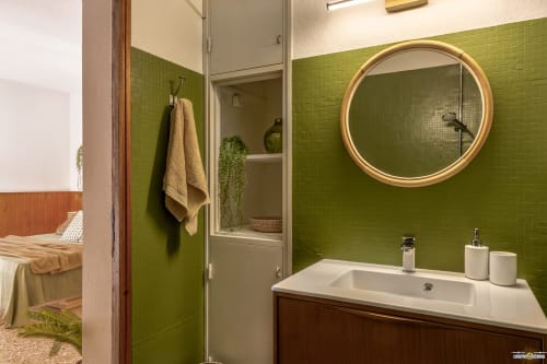 Salle de bains moderne aux murs carrelés verts, miroir rond doré, lavabo blanc et douche à l'italienne à La Conciergerie du Cap Corse