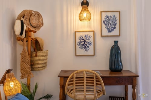 Espace de travail villa côtière avec bureau en bois, fauteuil en rotin, rangements tissés et œuvre corail bleu à La Conciergerie du Cap