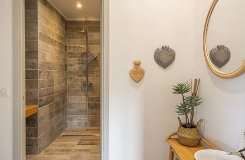 Salle de bains moderne avec douche à l'italienne, carrelage en pierre naturelle et accents muraux en forme de cœur à la Villa ANNONCIADE