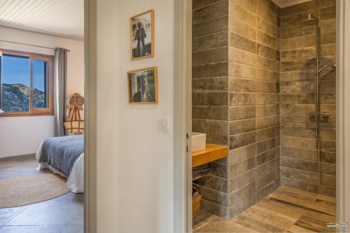 Salle de bain moderne avec douche en carrelage marron et paroi vitrée, ouvrant sur une chambre avec vue mer à La Conciergerie du Cap