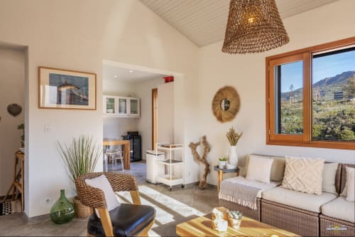 Salon moderne de villa à La Conciergerie du Cap Corse avec vue côtière montagnarde par grandes fenêtres, mobilier en rotin