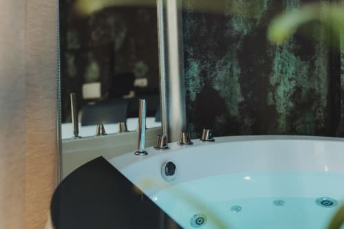 Vasca idromassaggio di lusso con finiture cromate e specchio in stile rustico nel bagno dell'esclusivo boutique hotel Oltre di Palermo