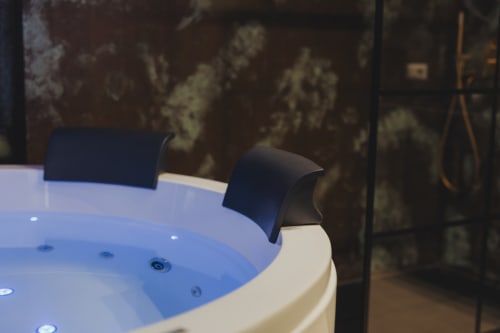 Vasca idromassaggio illuminata in blu presso l'hotel boutique esclusivo Oltre a Palermo, con muri in pietra rustica e poggiateste neri