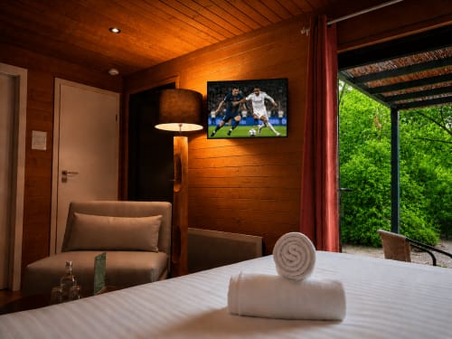 Modern lodge bedroom at Les Lodges de Vaugrigneuse with wooden walls, flat-screen TV, brown armchair, and garden view terrace