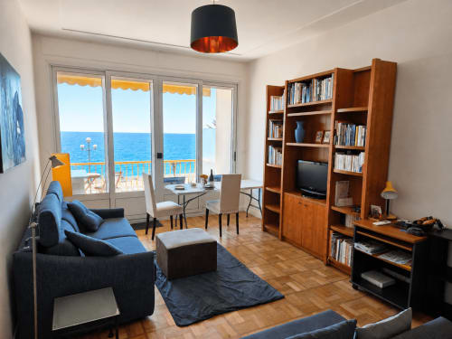 Bright seaside apartment in Nice with sea view balcony, comfortable seating, wooden shelving, TV, and modern black pendant